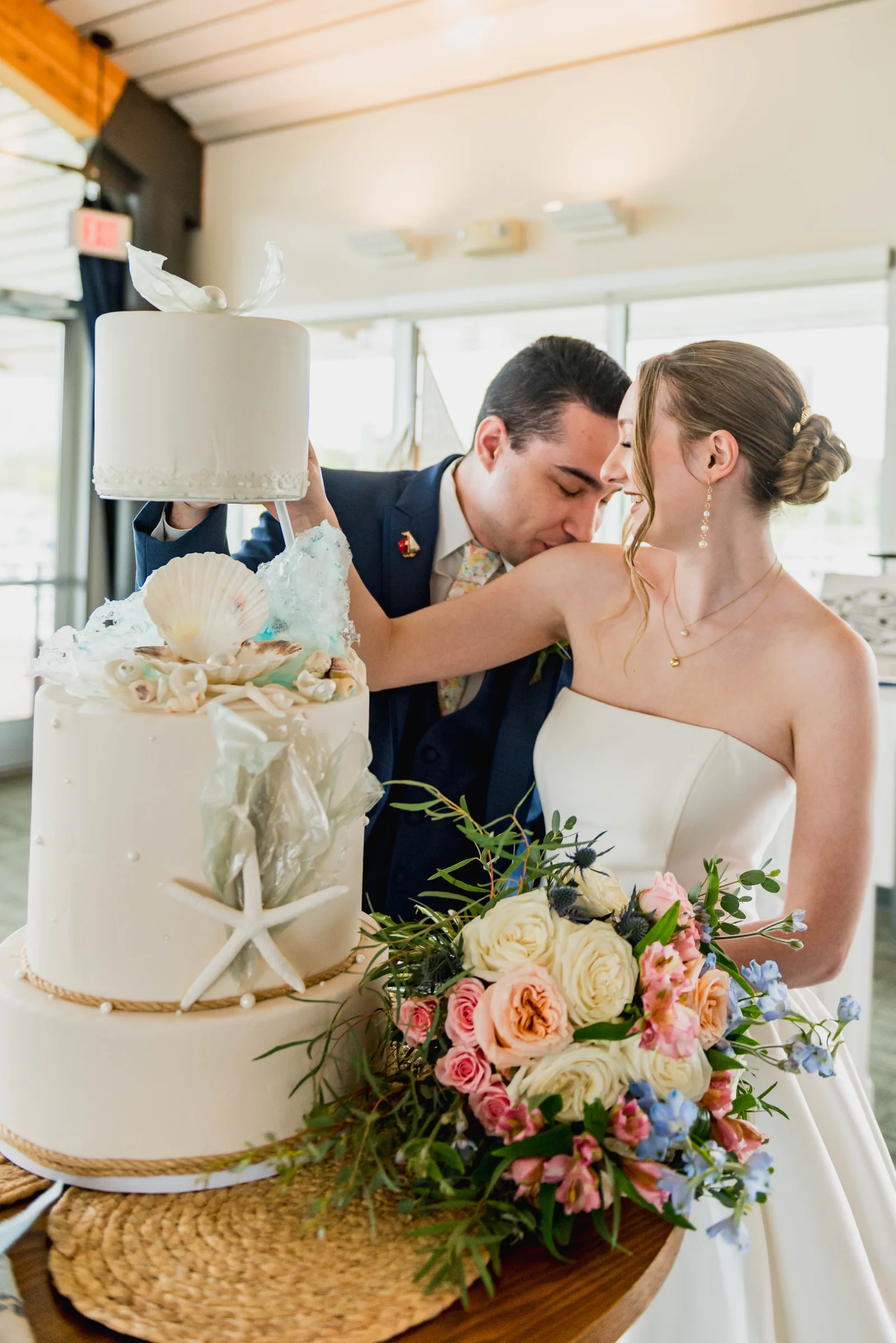 Casal de noivos ao lado de bolo de casamento com tema marinho